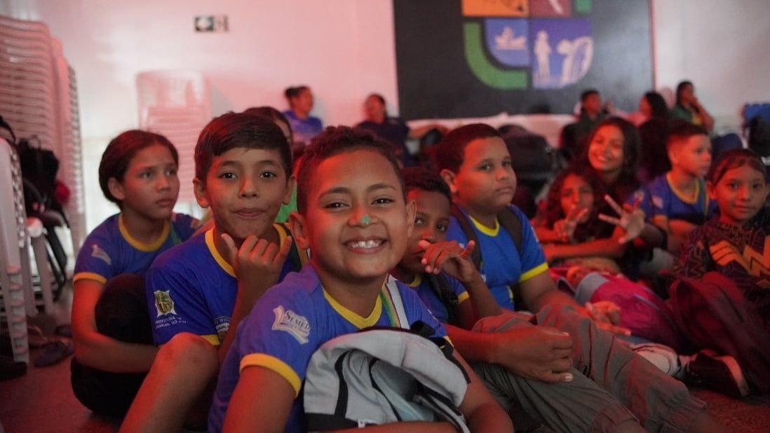 Crianças sorrindo sentadas no chão de uma sala de exibição