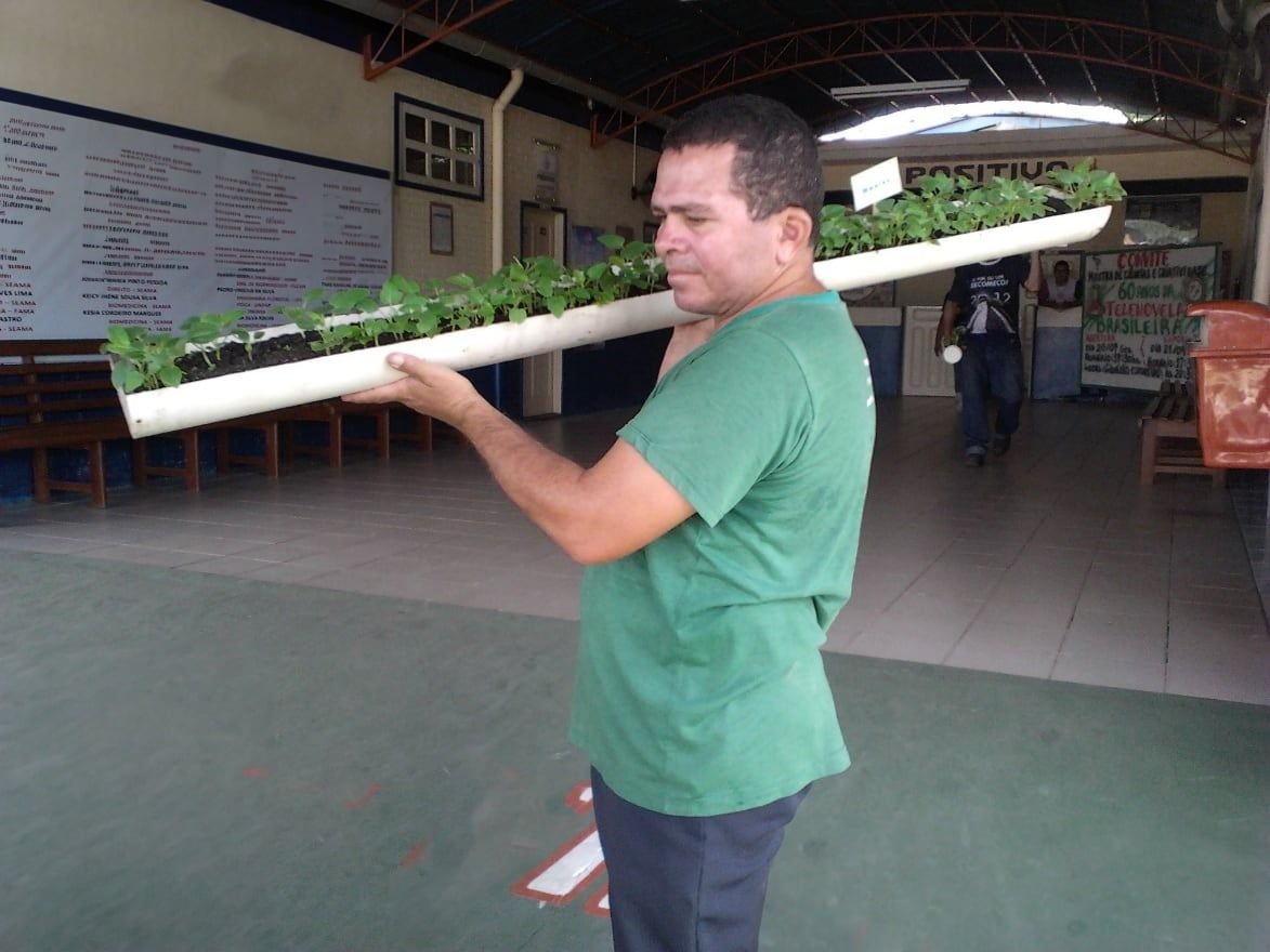 Homem segurando no ombro um tubo de PVC com mudas de hortaliças