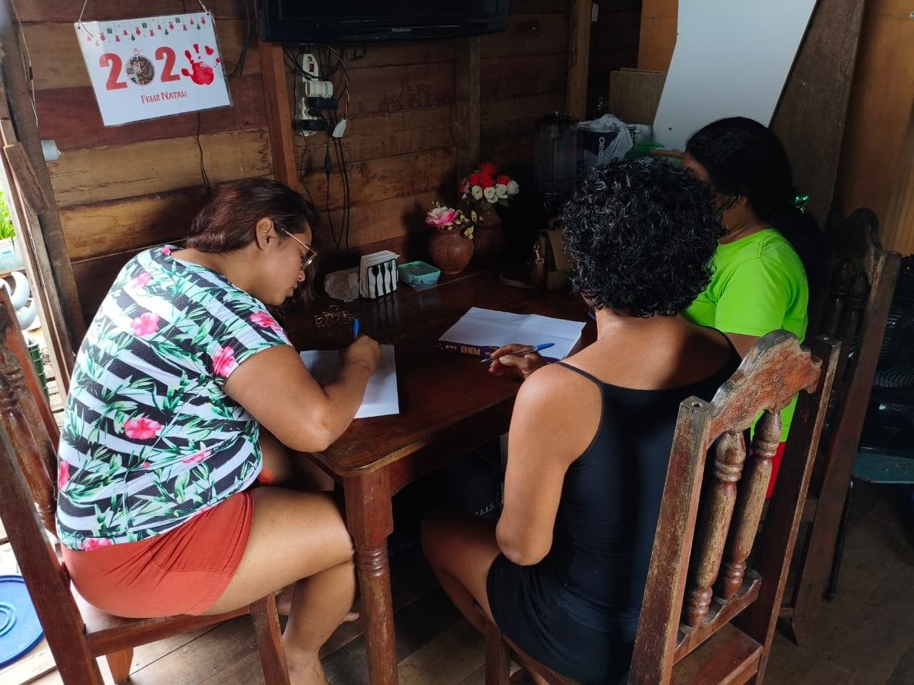 Mulheres escrevendo ao redor de uma mesa de madeira