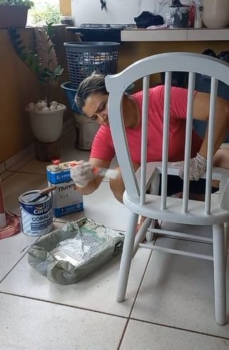 Pessoa pintando uma cadeira dentro de casa